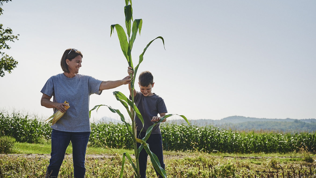 Une productrice de grandes cultures et son fils observent un plant de maïs en souriant. 