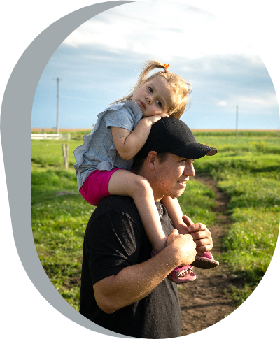 A Canadian farmer walks through a field with his little girl on his shoulders.