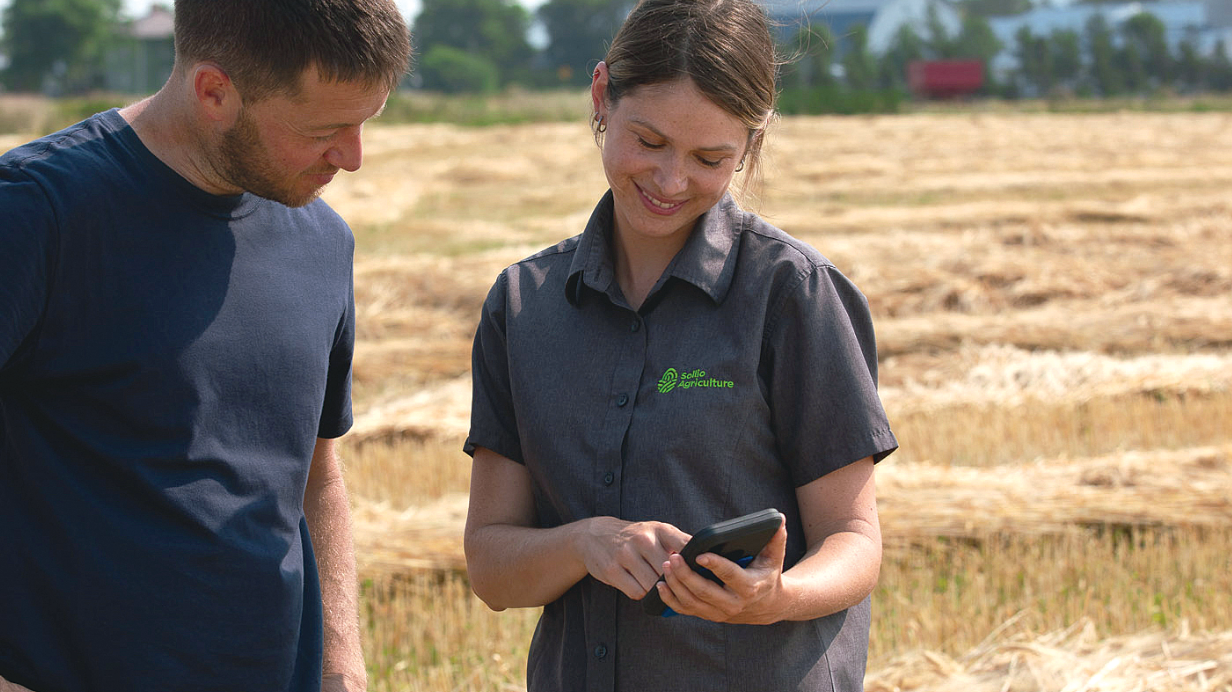 A farmer and a Sollio Agriculture agri-advisor consult a digital agriculture platform on a cell phone.