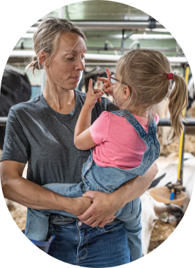 A farmer and her daughter in a barn with dairy cows.