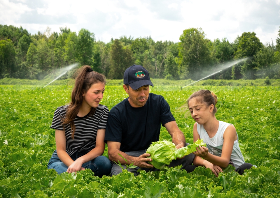 Un producteur et ses deux filles observent les effets positifs des biostimulants sur une laitue au champ. 