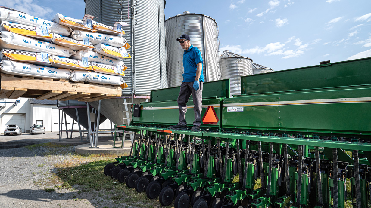 Un producteur agricole rempli son semoir avec des sacs de semences de maïs.