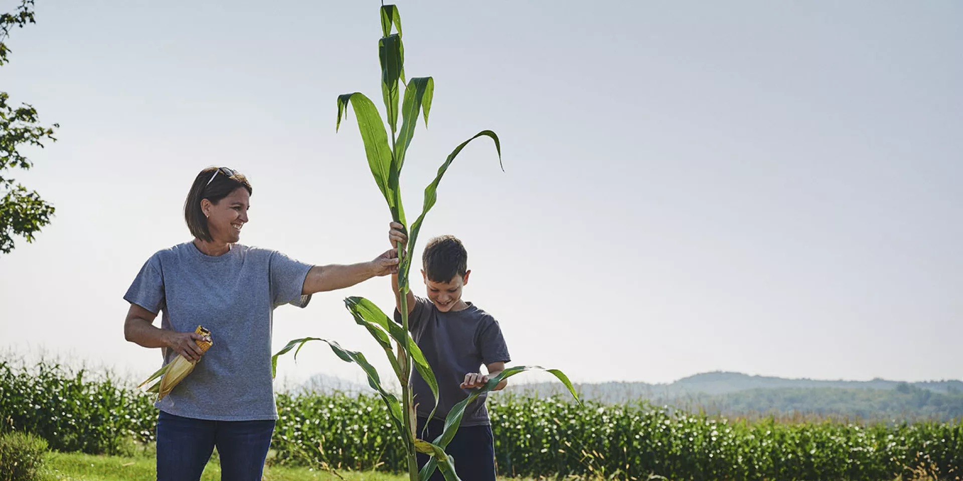 Une femme, à côté de son fils, tient un épi de maïs.