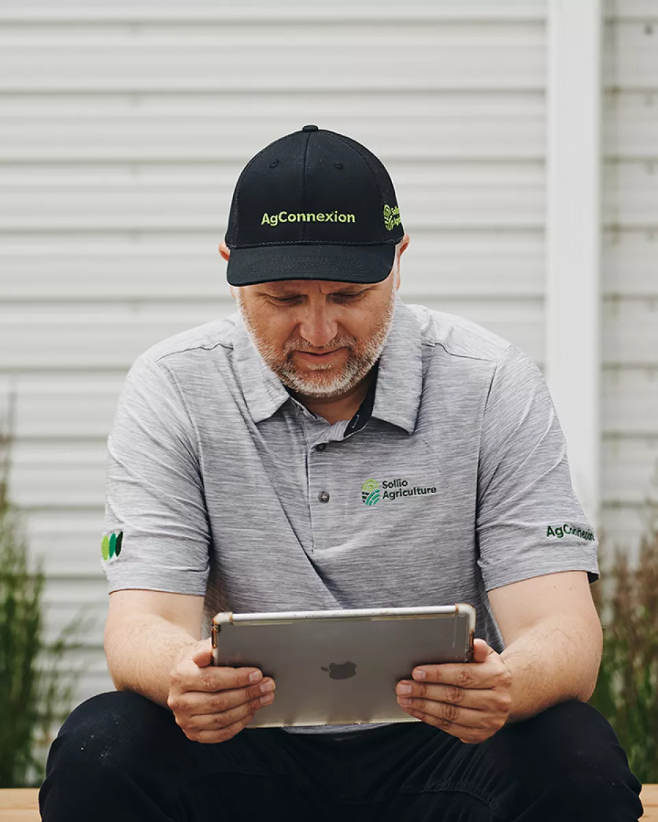 Un producteur, assis sur une marche de perron, consulte sa tablette.